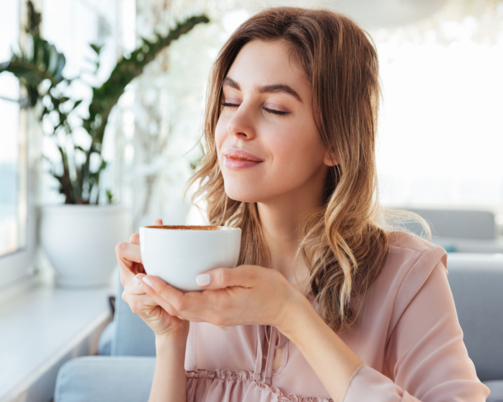 woman smiling while drinking and smelling coffee